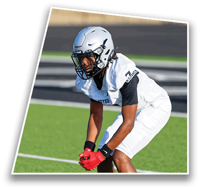 A person wearing a white football uniform and helmet is crouched on a green field, appearing ready to play. Description generated by AI
