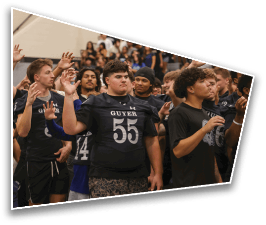 A group of people wearing sports jerseys and casual clothing are standing closely together with their hands raised in a gymnasium setting. Description generated by AI