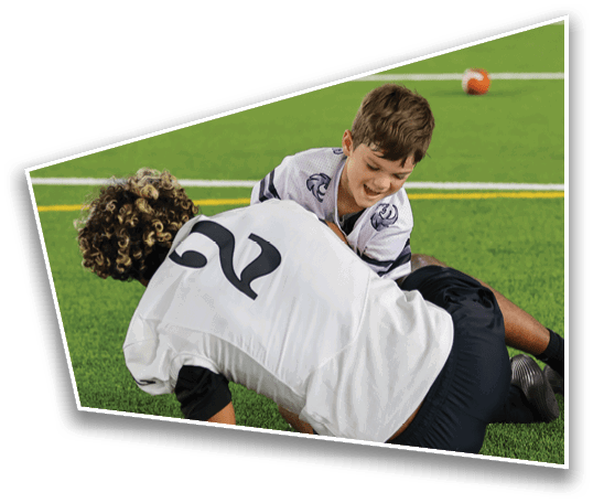 A child wearing a sports jersey is smiling and playing on a green football field with a football visible in the background. Description generated by AI