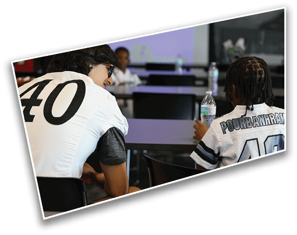 Two people wearing sports jerseys with the number 40 are seated and engaged in conversation in an indoor setting. Description generated by AI