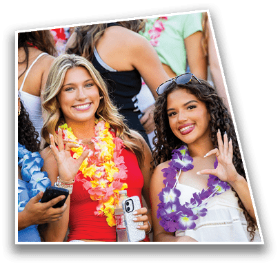 A group of people wearing colorful leis are gathered closely together, with one person in the foreground wearing a large silver bow in their hair. Description generated by AI
