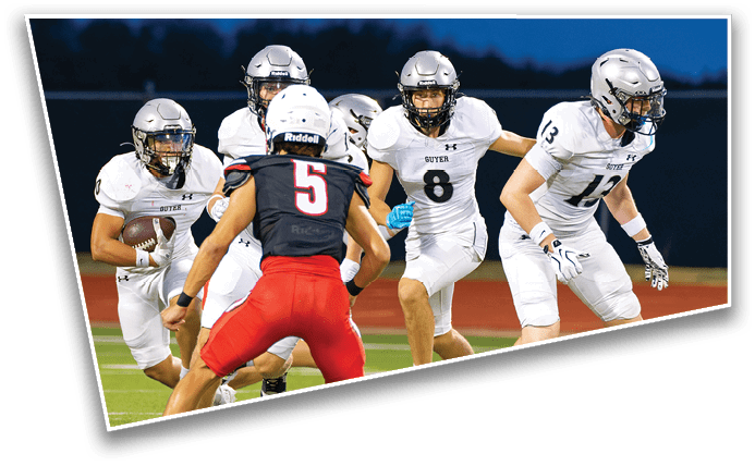 People wearing football uniforms are actively engaged in a play on a field, with one person holding the ball and others preparing to block or tackle. Description generated by AI