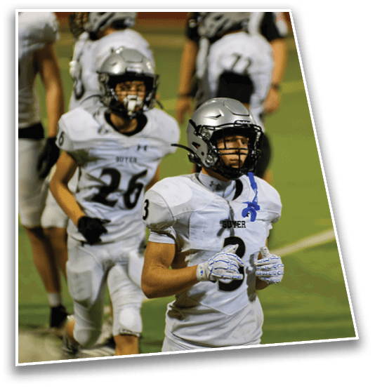 A person wearing a football helmet and white uniform with the number three stands on a field with another person blurred in the background. Description generated by AI