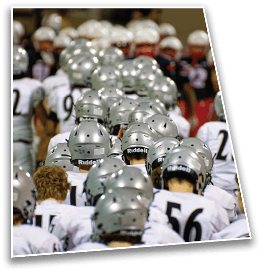 A group of people wearing silver football helmets and white uniforms are gathered closely together, facing away from the camera. Description generated by AI