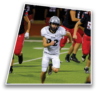 A person wearing a white football uniform and helmet is crouched on a green field, appearing ready to play. Description generated by AI