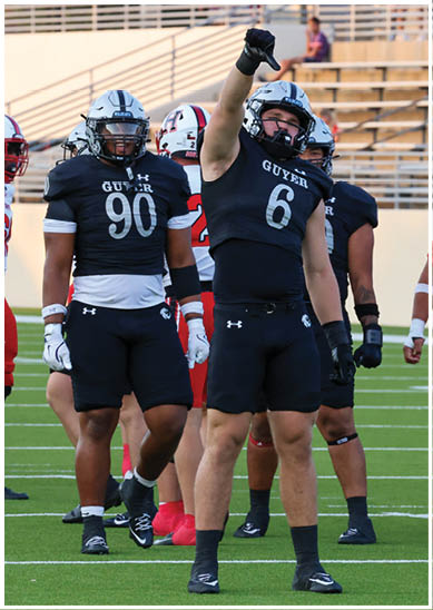 Several people wearing football uniforms stand on a field with one person in a black uniform raising an arm. Description generated by AI