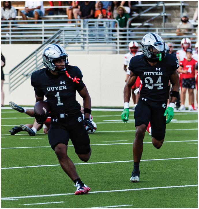 People sitting on bleachers watching a sporting event with two players wearing helmets visible in the foreground. Description generated by AI