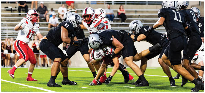 People wearing sports uniforms are engaged in a physical tackle on a green football field. Description generated by AI