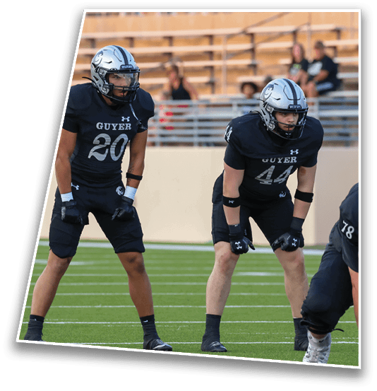 A person wearing a black football uniform with the number 44 is in a ready stance on a football field facing opponents in white and red uniforms. Description generated by AI