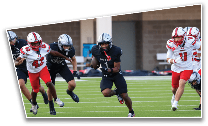 People in football uniforms are running on a field with one person in a black uniform holding a football while others in white and red uniforms chase. Description generated by AI