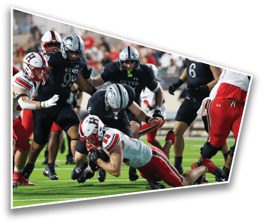 A group of people in football uniforms are engaged in a play on a field with one person in a white and red uniform diving forward while others in black uniforms attempt to tackle or block. Description generated by AI