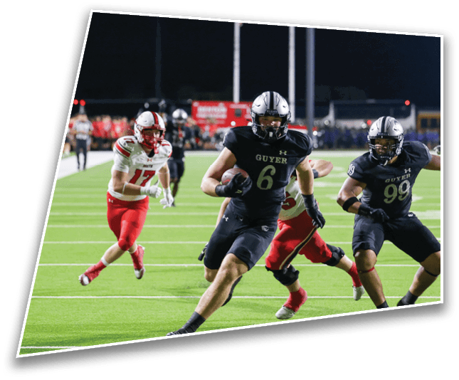 Players in black and red football uniforms are actively running on a green field during a nighttime game. Description generated by AI