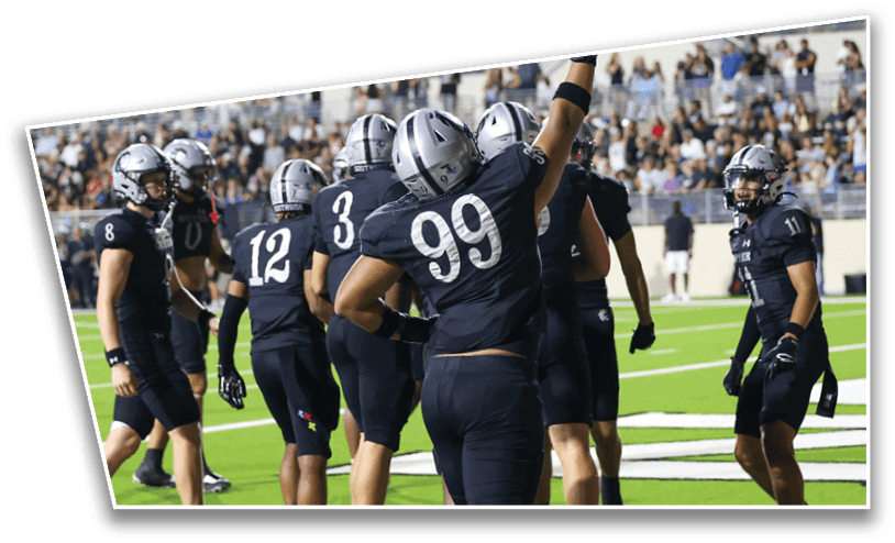 A group of people wearing black football uniforms and helmets are gathered on a green field with a crowd in the background. Description generated by AI