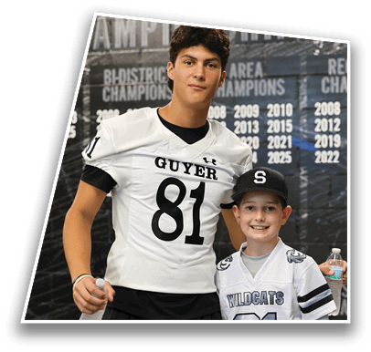 A person wearing a white football jersey with the number 81 and the word Guyer stands in front of a wall displaying championship years. Description generated by AI