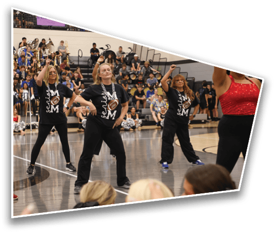Adults wearing matching black shirts and black pants are dancing on a gymnasium floor with an audience seated in the background. Description generated by AI