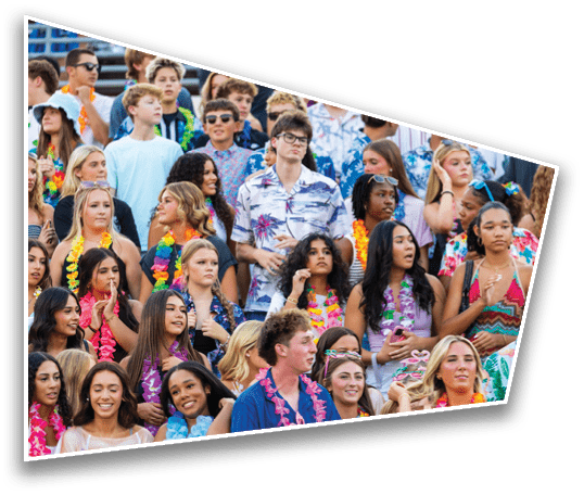 A large group of people wearing colorful leis and casual clothing are gathered closely together, some smiling and others looking in different directions, suggesting a festive outdoor event. Description generated by AI