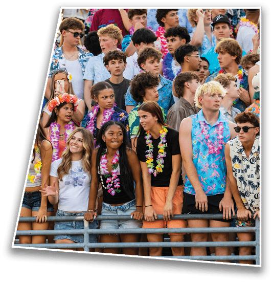 A group of people wearing colorful Hawaiian shirts and leis are standing closely together behind a railing, appearing to be at a festive outdoor event. Description generated by AI