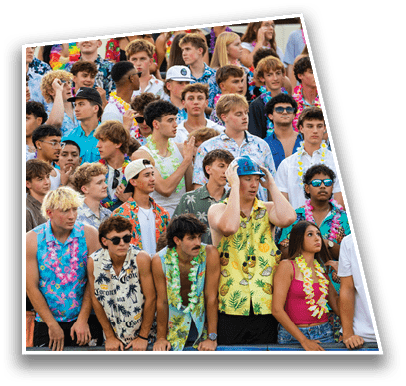 A large group of people wearing colorful tropical shirts and leis are gathered closely together, some looking excited and others focused, suggesting a festive or sporting event. Description generated by AI