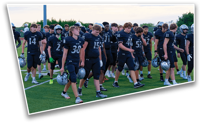 A group of people wearing black football uniforms and holding helmets are standing together on a sports field. Description generated by AI