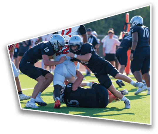 Several people wearing football uniforms are engaged in a tackle on a grassy field during a game. Description generated by AI