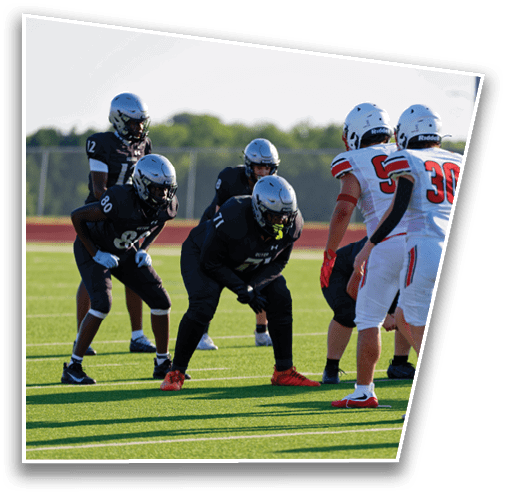 People in sports uniforms are positioned on a football field preparing for a play, with one person holding a football ready to snap it. Description generated by AI
