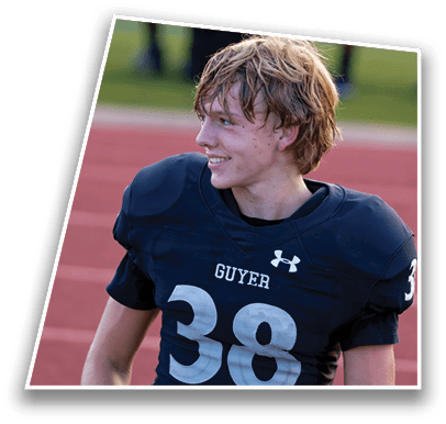 A person wearing a dark blue football jersey with the number 38 and the word “GUYER" on the front stands on a red track background. Description generated by AI