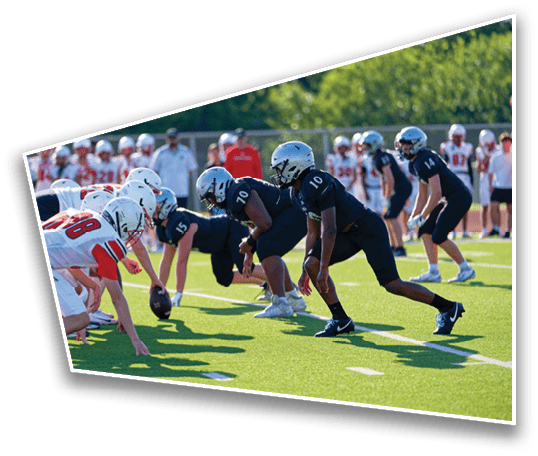 Two opposing American football teams are lined up at the line of scrimmage on a sunny field with players in black and white uniforms preparing for the next play. Description generated by AI