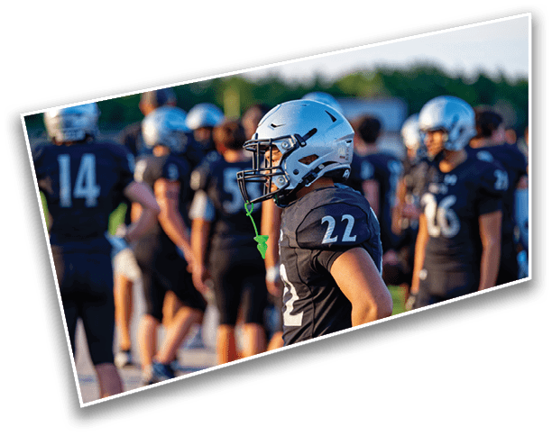 A person wearing a silver football helmet and black jersey with the number 22 stands on a field with other similarly dressed people in the background. Description generated by AI