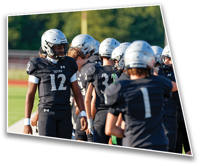 A group of people wearing black football uniforms and silver helmets are standing on the sidelines of a football field. Description generated by AI
