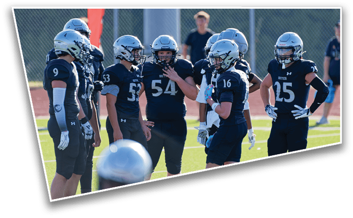 A group of people wearing black football uniforms and helmets are standing together on a field, seemingly discussing strategy during a game. Description generated by AI