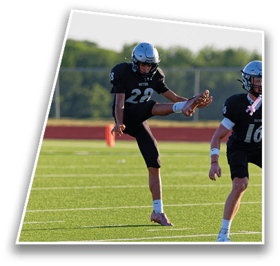 Two people in football uniforms are on a field with one person kicking a ball and the other running beside them. Description generated by AI