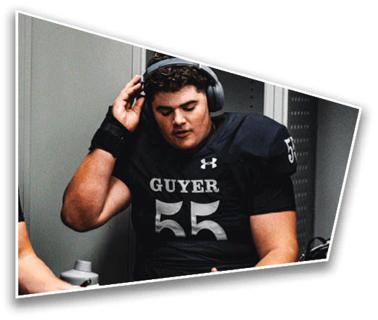 A person wearing a football uniform with the number 55 and the word Guyer is adjusting headphones while standing in a locker room. Description generated by AI
