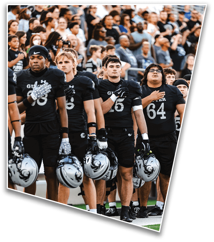 People in football uniforms stand with their hands over their hearts in front of a crowd at a sports event. Description generated by AI