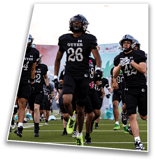 People in black football uniforms with helmets are running on a field during a game or practice. Description generated by AI