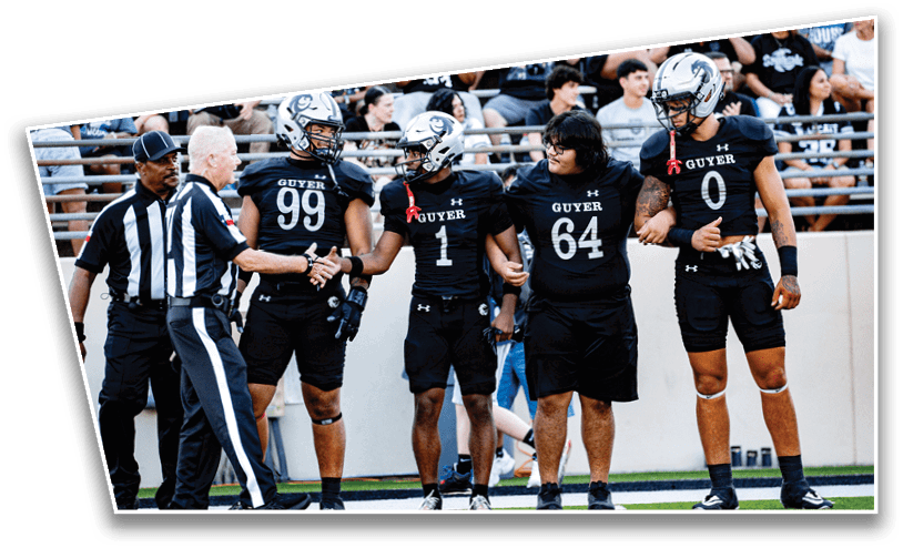 Four athletes in football uniforms and a referee stand linked arm-in-arm on a field, preparing for a game. Description generated by AI