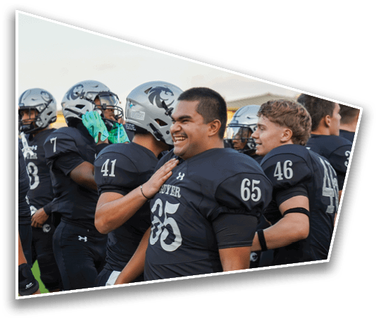A group of people wearing black football uniforms and helmets are standing together on a field, with one person smiling and another placing a hand on their shoulder. Description generated by AI