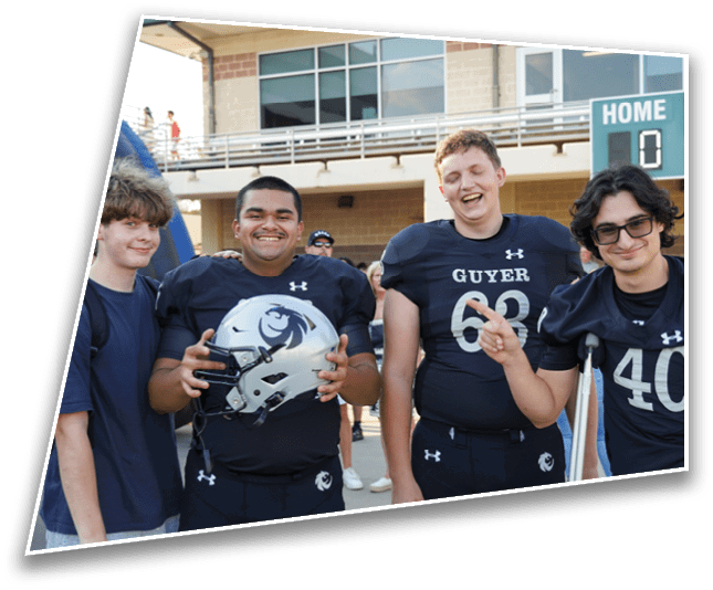 Three people wearing football uniforms stand together outside a building near a scoreboard, with one holding a helmet and another using crutches. Description generated by AI