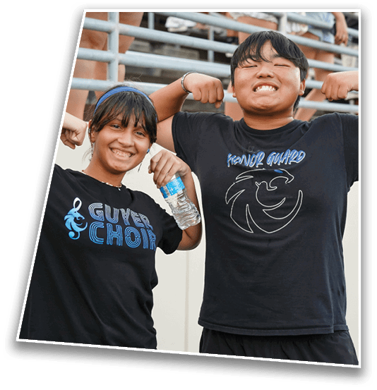 Two people smiling and posing with one person flexing their arms and the other holding a water bottle, both wearing black t-shirts with text and graphics. Description generated by AI