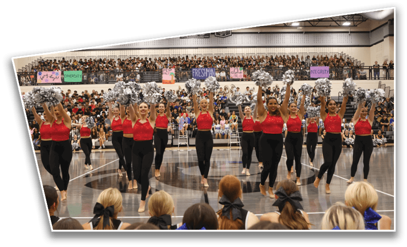 A group of adults in red tops and black pants perform a synchronized cheerleading routine with silver pom-poms in a gymnasium filled with seated spectators. Description generated by AI