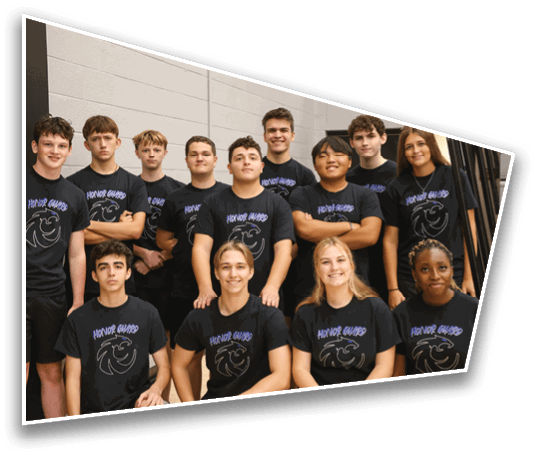 A group of people wearing matching black t-shirts with a logo and the words “Honor Guard" pose together indoors against a light-colored wall. Description generated by AI