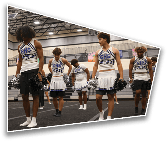 A group of people wearing cheerleading uniforms with “GHS" on the front are standing in a gymnasium holding pom-poms. Description generated by AI