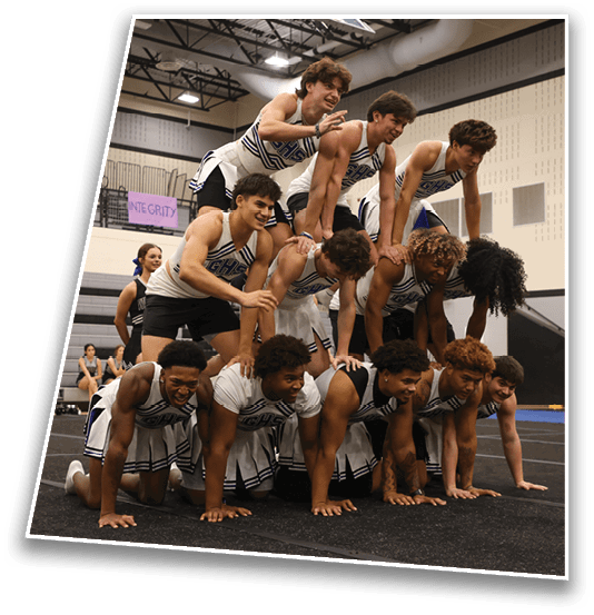 A group of people wearing matching cheerleading uniforms are forming a human pyramid inside a gymnasium. Description generated by AI