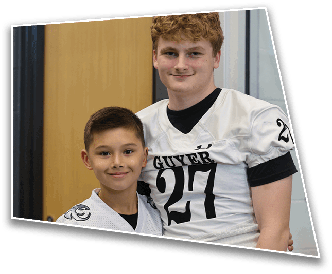 Two people are smiling indoors, with one wearing a sports jersey that says “GUYER" and the other partially visible in front. Description generated by AI