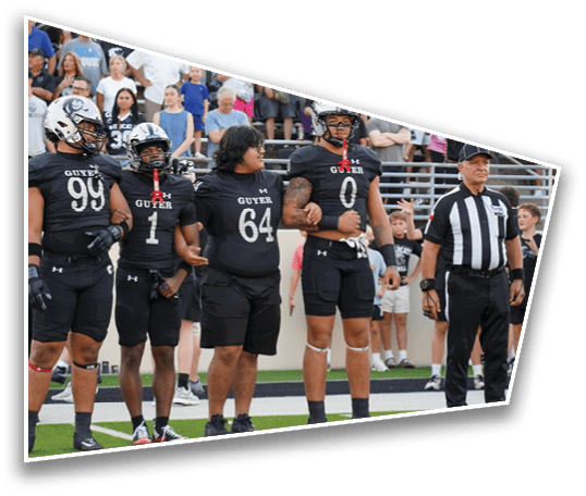Several people in football uniforms and a referee stand on a field with spectators in the background. Description generated by AI