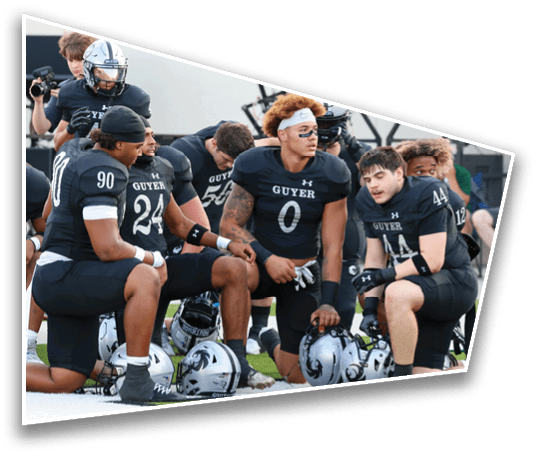 A group of people wearing black football uniforms with helmets on the ground are kneeling and sitting on a sports field. Description generated by AI