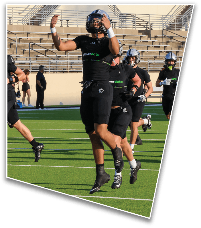 People in black sports uniforms are running and jumping on a green football field with empty bleachers in the background. Description generated by AI