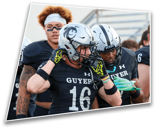 Three people in football uniforms with helmets and gloves are preparing on the sidelines during a game or practice. Description generated by AI