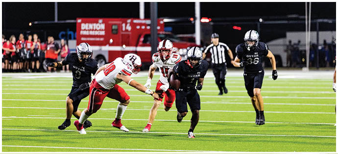 People in football uniforms are actively running and competing on a brightly lit field during a night game. Description generated by AI