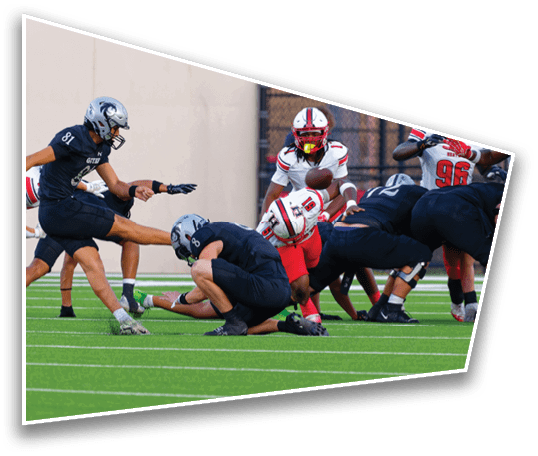Several people in football uniforms are positioned on a field preparing for a play, with one person holding the ball and others crouched or standing in formation. Description generated by AI