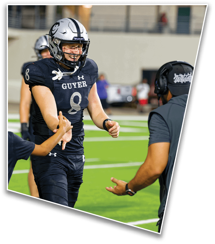 A person in a football uniform with the number 8 is smiling and giving a thumbs-up while interacting with two other people on a football field at night. Description generated by AI